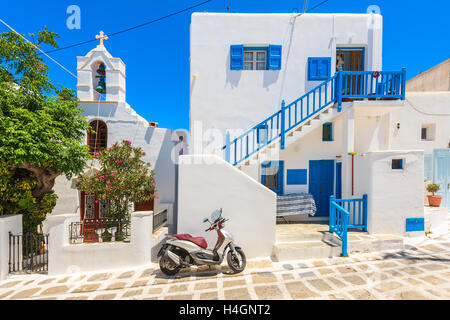 La ville de Mykonos, Grèce - 16 MAI 2016 : Scooter stationné sur une rue en face d'une maison grecque blanche typique et de l'église, l'île de Mykonos Banque D'Images
