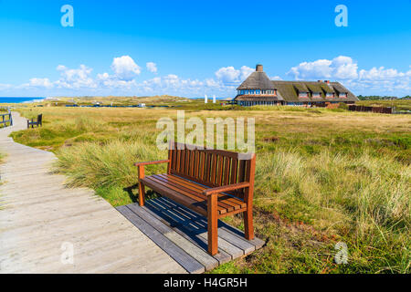 Banc sur sentier pédestre le long d'une côte de l'île de Sylt et guest house typique frison en arrière-plan, Allemagne Banque D'Images