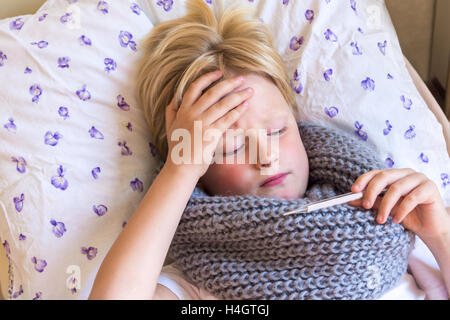 Sick little boy holding pose thermomètre au lit avec visage triste - santé et médecine concept Banque D'Images