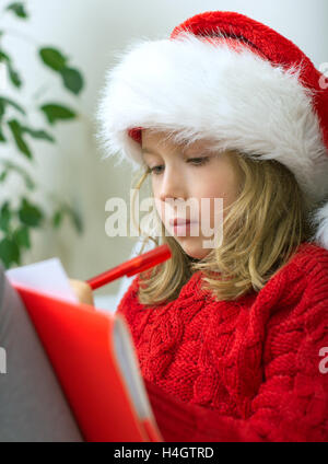 Petite fille dans red hat écrit une lettre au Père Noël. Banque D'Images
