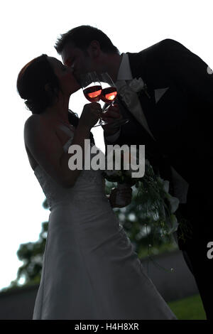 Kissing couples nuptiales avec verres à vin rouge comme une silhouette Banque D'Images