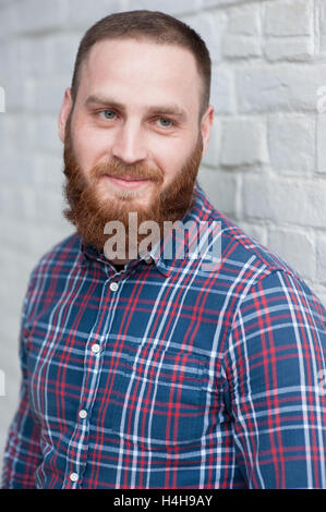 Portrait de jeune homme barbu portant flanelle devant white brick wall Banque D'Images