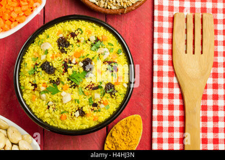 Couscous aux légumes dans un bol noir, avec une fourche en bois, une serviette et quelques ingrédients et épices Banque D'Images