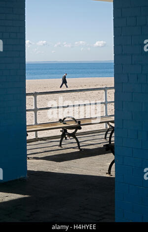 Un homme solitaire marche sur une étendue de plage isolée à Coney Island, Brooklyn, New York Banque D'Images