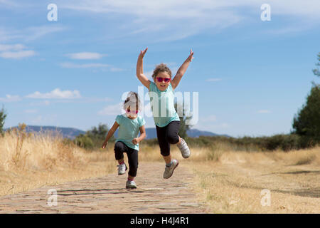 Portrait de petites filles dans le saut d'usure similaires tenant la main dans la main le long du chemin de pierre dans le parc. Banque D'Images