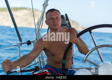 Jeune homme skipper steers la roue de yacht à voile. Location, vacances, voyage. Banque D'Images