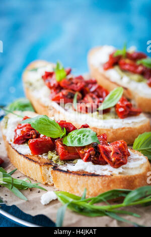 Bruschetta au fromage à la crème, le pesto, basilic frais et tomates séchées au soleil sur une table en bois rustique bleu Banque D'Images