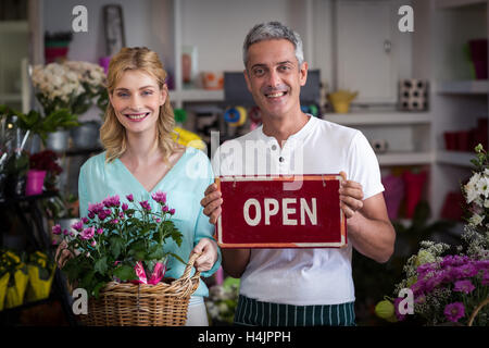 Les fleuristes holding open sign plaque et panier de fleurs in flower shop Banque D'Images