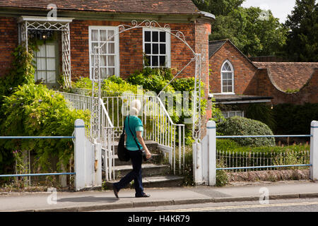L'Angleterre, Berkshire, Hungerford, High Street, woman walking passé maison avec passerelle de porte d'entrée à côté du canal de Kennet et Avon Banque D'Images