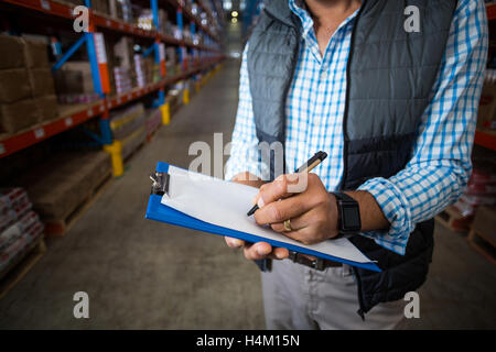 Mid section of warehouse worker writing on clipboard Banque D'Images