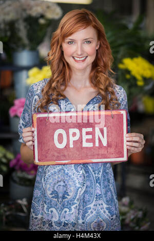 Les fleuristes Smiling holding open sign placard in flower shop Banque D'Images