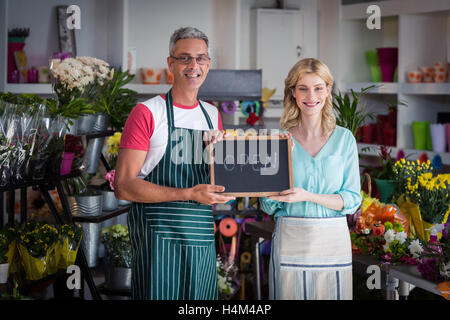 Les fleuristes Smiling holding open sign sur ardoise in flower shop Banque D'Images