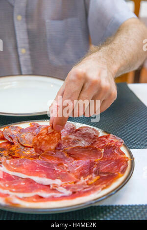 La main de l'homme ayant une assiette de chorizo ibérique de variétés de produits. L'Espagne. Banque D'Images