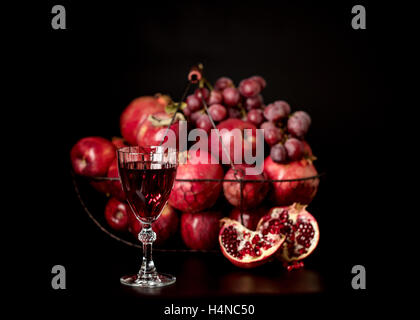 Nature morte sur un fond sombre. (Vin) verres d'alcool, de fruits et de petits fruits (pommes, raisins et grenades) dans le panier. Banque D'Images