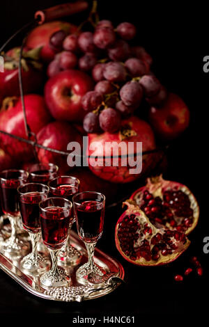 Nature morte sur un fond sombre. (Vin) verres d'alcool, de fruits et de petits fruits (pommes, raisins et grenades) dans le panier. Banque D'Images