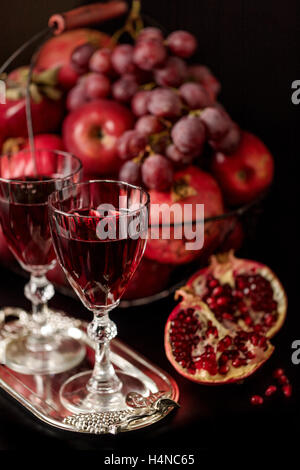 Nature morte sur un fond sombre. (Vin) verres d'alcool, de fruits et de petits fruits (pommes, raisins et grenades) dans le panier. Banque D'Images