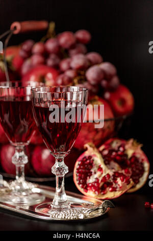 Nature morte sur un fond sombre. (Vin) verres d'alcool, de fruits et de petits fruits (pommes, raisins et grenades) dans le panier. Banque D'Images