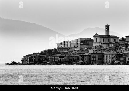 Lointain petit village de pêcheurs sur le lac de Côme en Italie au bord de l'eau calme face aux montagnes des Alpes en arrière-plan. Banque D'Images