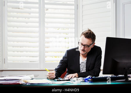 Un homme assis à un bureau dans office, de travailler, de tenir un crayon. Banque D'Images