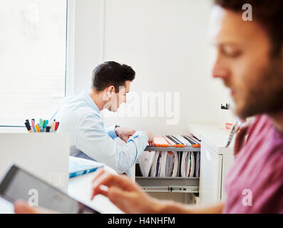 Un homme à la recherche grâce aux fichiers office, et un homme en utilisant sa tablette numérique. Banque D'Images