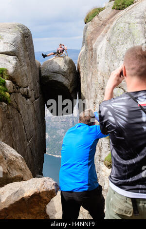 Les touristes de prendre des photos d'un ami, assis dans une chaise de plage dangereusement avec une canette de bière sur Kjeragbolten, un rock hanging 1100 mètres au-dessus du fjord Lysefjorden, Norvège Banque D'Images