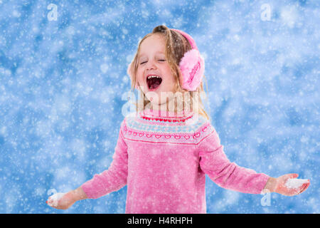 Funny little girl dans un chapeau tricoté coloré et manteau chaud jouant avec la neige. Les enfants jouer dehors en hiver. Banque D'Images