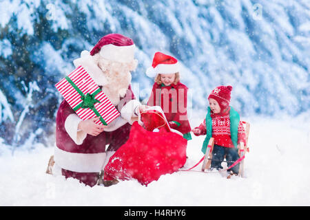 Le Père Noël et les enfants de l'ouverture présente dans la forêt enneigée. Les enfants et le père à Santa costume et beard ouvrir les cadeaux de Noël. Banque D'Images