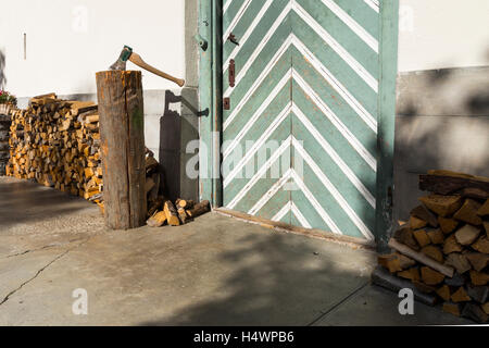 Détail d'un bâtiment rural : une porte en bois verdâtre avec des rayures blanches, bois empilés et un couperet avec une hache. Banque D'Images