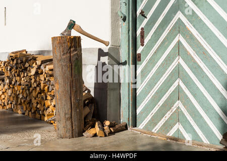 Détail d'un bâtiment rural : une porte en bois verdâtre avec des rayures blanches, bois empilés et un couperet avec une hache. Banque D'Images