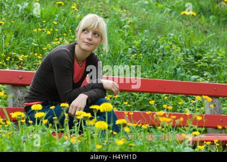 Jeune femme assise sur un banc sur une prairie de printemps Banque D'Images