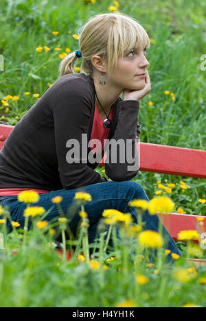 Jeune femme assise sur un banc sur une prairie de printemps Banque D'Images