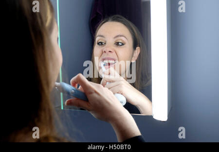 Jeune femme à la recherche dans la salle de bains miroir car elle nettoie les dents avec brosse à dents électrique Banque D'Images