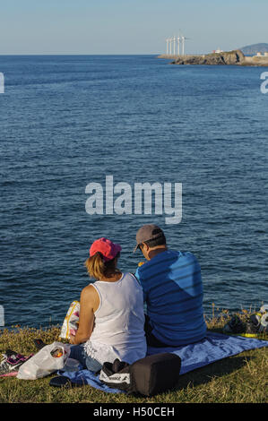 Adult couple eating chips assise sur le bord d'une falaise surplombant la baie de Biscaye, Pays Basque, Espagne, Europe Banque D'Images