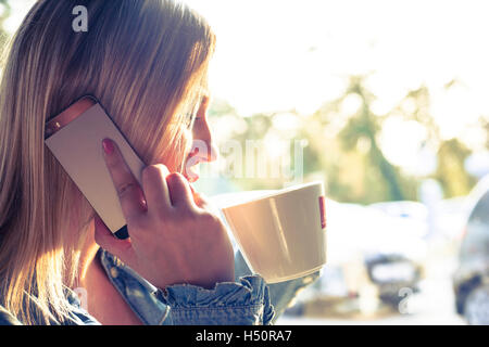 Jeune femme à boire le café et talking on mobile phone Banque D'Images