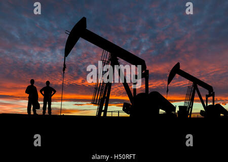 Silhouette d'ouvriers du pétrole dans un champ pétrolifère pumpjack site contre un ciel dramatique. Banque D'Images