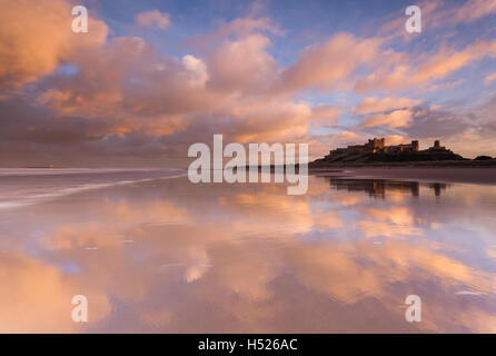 Bamburth castle et plage sur la côte de Northumberland au coucher du soleil, avec les nuages reflètent dans l'eau sur le sable que la marée se Banque D'Images