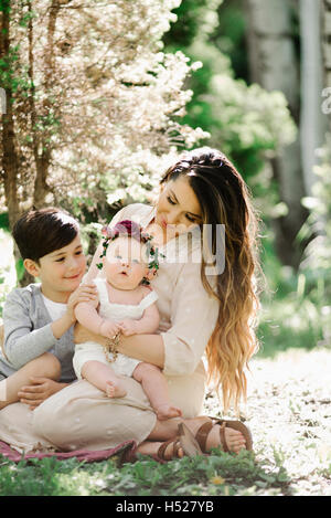 Portrait of a smiling mother, garçon et fille avec une couronne de fleurs sur la tête, assis dans un jardin. Banque D'Images