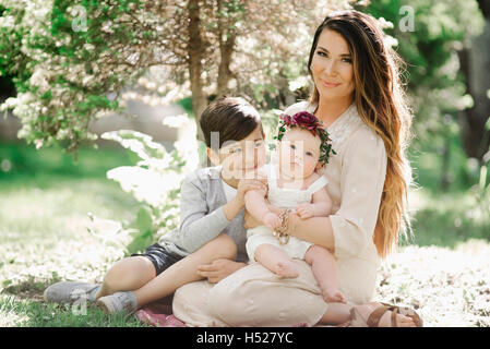 Portrait of a smiling mother, garçon et fille avec une couronne de fleurs sur la tête, assis dans un jardin. Banque D'Images