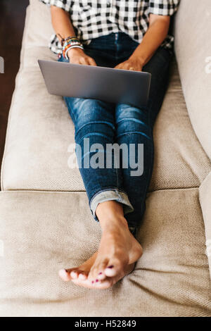 Le port de jeans femme couchée sur un canapé, à l'aide d'un ordinateur portable. Banque D'Images