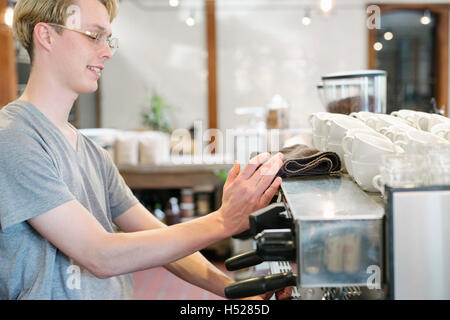 Jeune homme blond avec des lunettes à la machine espresso dans un café. Banque D'Images