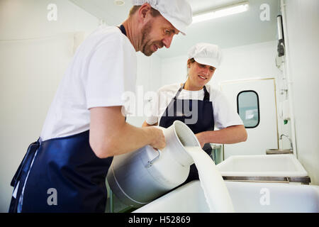 L'homme et la femme dans une crémerie, verser le lait de chèvre à partir d'un fromage de chèvre, de désabonnement. Banque D'Images