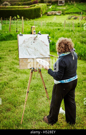 Une femme à l'extérieur à l'artiste, l'application de peinture de chevalet sur papier avec un pinceau. Banque D'Images