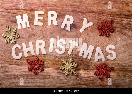 Joyeux Noël avec des lettres en bois sur le bois avec de l'or et rouge décorations flocon Banque D'Images
