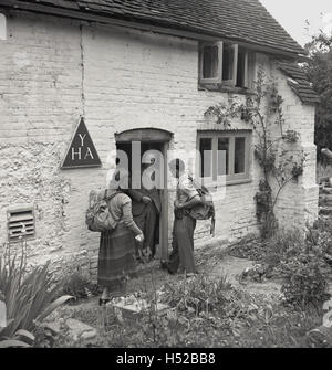 Années 1950, historiques, marcheurs ou randonneurs avec cartables sur le dos, parler à un homme qui court un YHA (Youth Hostel Association) cottage. Banque D'Images