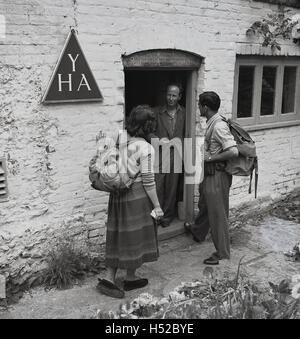 Années 1950, historiques, deux marcheurs ou randonneurs avec cartables sur le dos, parler à un homme qui court un YHA (Youth Hostel Association) cottage. Banque D'Images