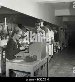 Années 1950, historiques, d'immigrants nouvellement arrivés de l'étranger la Grande-Bretagne payant à un jusqu'à son repas dans une cafétéria self-service, Londres, Angleterre. Banque D'Images