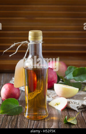 Le vinaigre de cidre de pomme dans une bouteille en verre avec des pommes sur une table dans un style rustique. Banque D'Images
