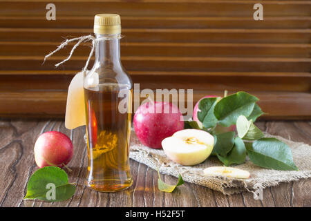 Le vinaigre de cidre de pomme dans une bouteille en verre avec des pommes sur une table dans un style rustique. Banque D'Images