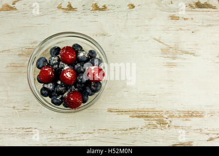 Bleuets et framboises saupoudrées de sucre glace dans un bol en verre sur une vieille table en bois clair, dans un style vintage , spa copie Banque D'Images