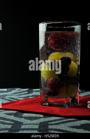 L'eau pétillante avec framboises, bleuets et raisins dans un verre haut et serwetve rouge sur fond noir. Clairement visible g Banque D'Images